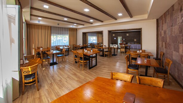 Un comedor espacioso con mesas y sillas de madera, un techo alto con vigas a la vista y grandes ventanales que permiten la entrada de luz natural.