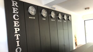 Zona de recepción con una pared negra que exhibe relojes con nombres de ciudades como Moscú, París y Nueva York.