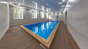 Una piscina interior con solárium de madera, amplias ventanas y pared de azulejos.