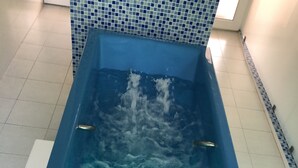 Un jacuzzi azul con múltiples chorros y mandos, sobre un suelo y una pared de azulejos.