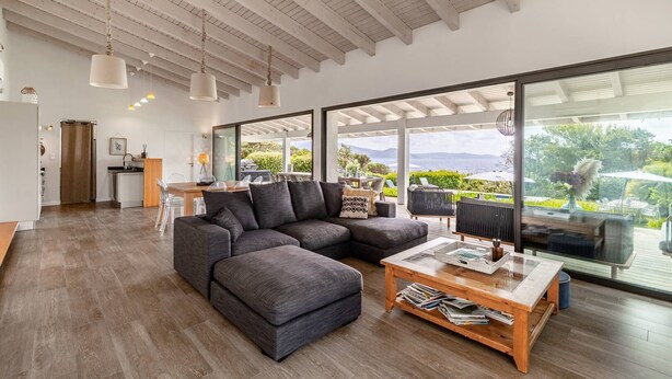 Amplia sala de estar con un sofá seccional grande, una mesa de centro de madera y vistas al exterior a través de amplios ventanales.