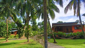 A tropical garden with palm trees, a hammock, and a building with a red roof. - Beachfront Villa Seabreeze with AC & Pool (Puerto Viejo)