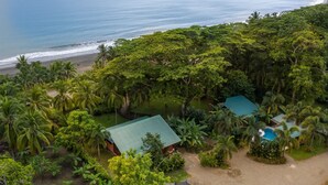 A tropical resort with a beach view, dense greenery, and a small building with a green roof. - Beachfront Villa Seabreeze with AC & Pool (Puerto Viejo)