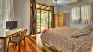 A bedroom with a bed, a desk with a chair, a TV, and a window with curtains.
