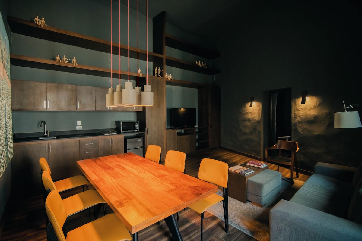 A modern kitchen with wooden cabinets, a dining table with chairs, and pendant lighting.