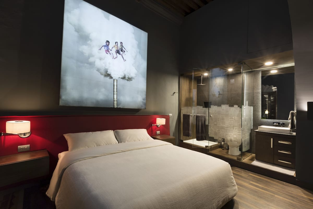 A hotel room with a bed, a large wall-mounted TV, a glass-enclosed shower, and a modern bathroom.
