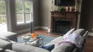 A living room with a fireplace, a television mounted on the wall, and a large window. - Beautiful Home close to campus (Oxford)