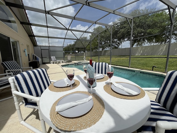 An outdoor patio with a pool, covered seating, and a table set for two with wine glasses.