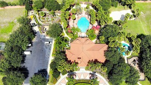 Luchtbeeld van een resort met een centraal gelegen zwembad, een tennisbaan en een parkeerplaats.