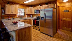 Cocina estilo cabaña de madera con encimeras de granito, electrodomésticos de acero inoxidable y armarios de madera.