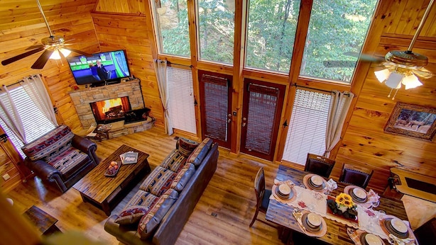 Interior acogedor de una cabaña con chimenea de piedra, televisor, sofá y mesa de comedor preparada para cuatro personas.