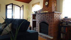 A living room with a brick fireplace, a sofa, a bookshelf, and a window with a view.