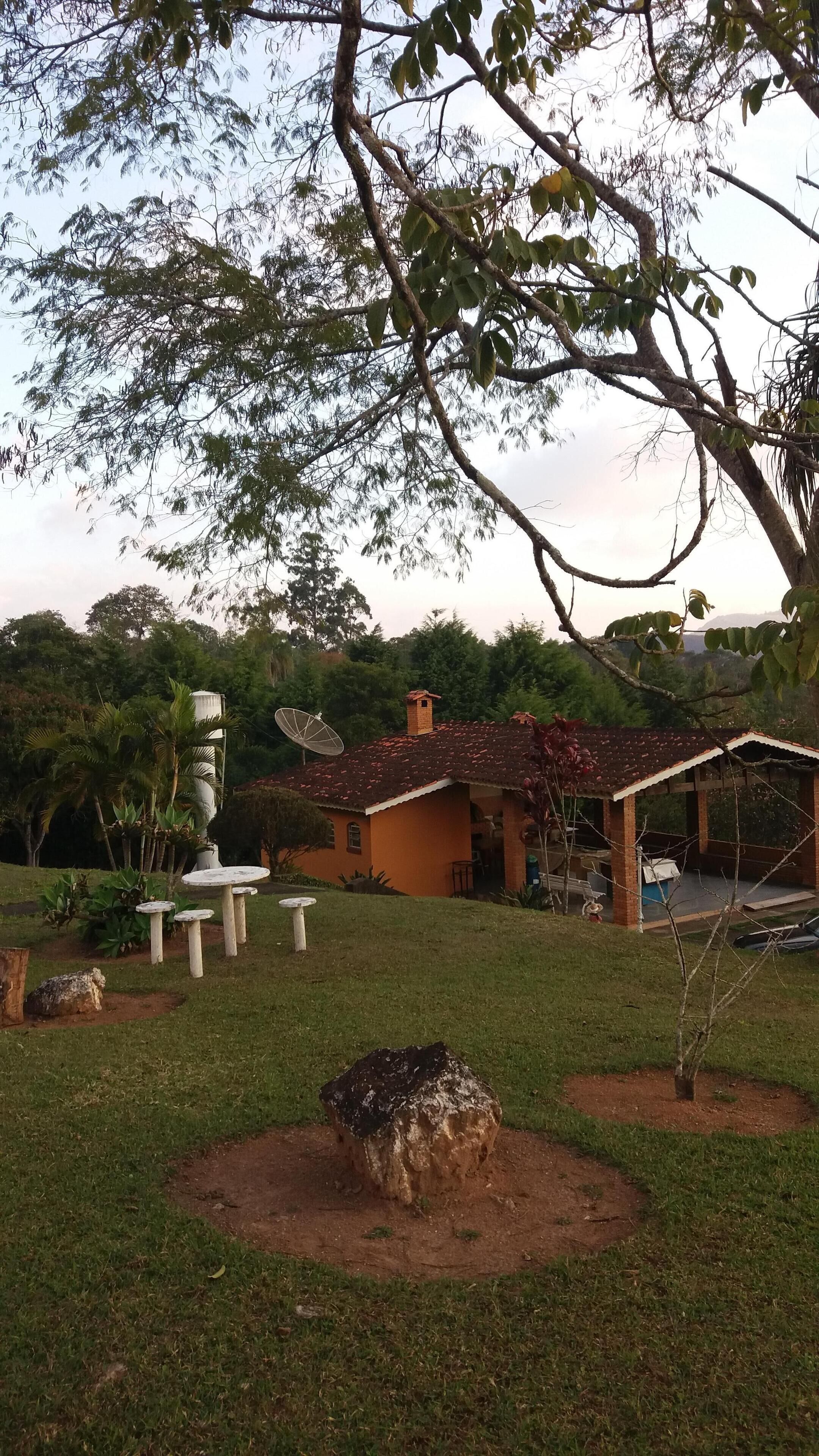 Ein rustikales Haus mit Ziegeldach, umgeben von einem gepflegten Garten mit einem großen Baum, einem Felsen und einer Satellitenschüssel.