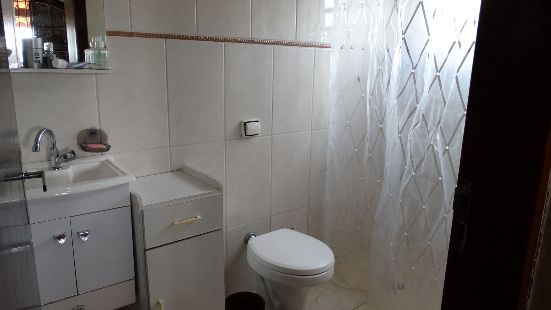 A small bathroom with a sink, mirror, and toilet. There are toiletries on the sink counter.