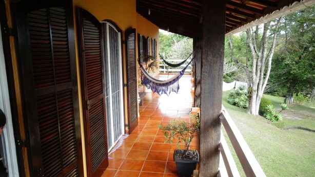 A covered outdoor area with a hammock, tiled flooring, and a view of a garden.