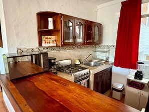 Une cuisine de taille réduite, dotée d’un plan de travail en bois, d’une cuisinière à gaz, d’un évier et d’un rideau rouge.