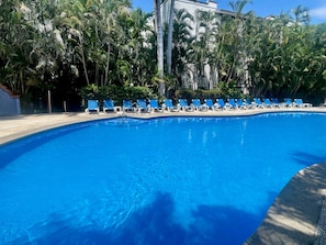 Une piscine d’un bleu éclatant, avec des chaises longues et des palmiers en arrière-plan.