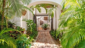 A narrow brick pathway flanked by lush green foliage, leading to a building entrance marked with the number 13.