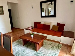 A living room with a sofa, a coffee table, and a small table with a potted plant.
