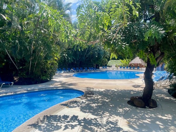 A pool area with multiple swimming pools, lounge chairs, and tropical vegetation.