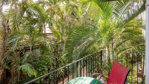 A balcony with a metal railing, surrounded by lush green foliage, including palm trees and other tropical plants.