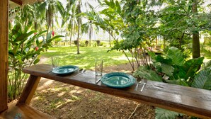 A wooden table with two green plates, a glass, and cutlery set outdoors, surrounded by lush greenery and palm trees. - Beachfront Villa Starfish with AC & Pool (Puerto Viejo)