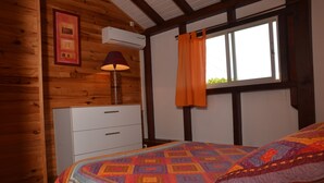 Habitació amb panells de fusta, un llit, un armari, un aparell d'aire condicionat i una finestra amb cortines.