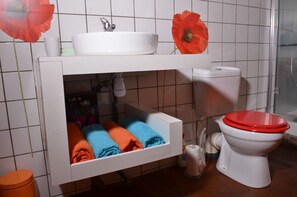 A bathroom with a white sink, toilet, and shower. There are towels in a cabinet and a toilet paper holder. - HIBISCUS AND ITS PANORAMIC SEA VIEW (SAINTE-ANNE)