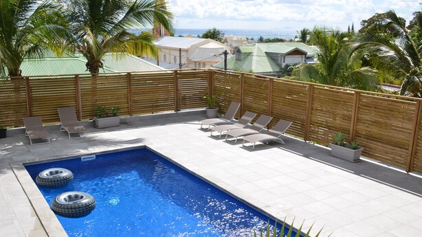 Piscina rectangular amb dues camèns inflables, envoltada per una tanca de fusta, amb gandules i plantes en testos.