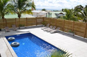 A rectangular swimming pool with two inflatable tires, surrounded by a wooden fence, with lounge chairs and potted plants. - HIBISCUS AND ITS PANORAMIC SEA VIEW (SAINTE-ANNE)