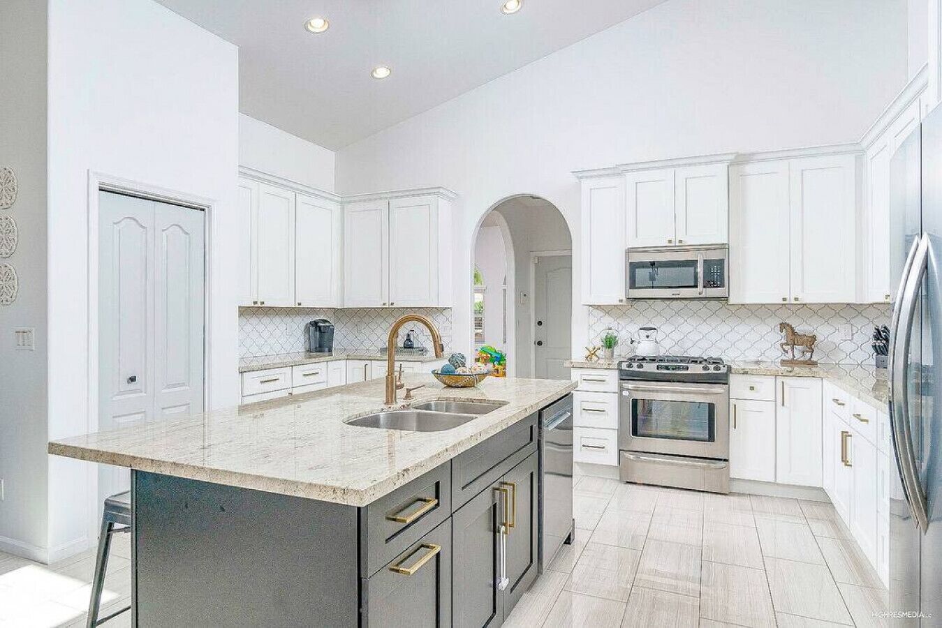 Una cocina moderna con armarios blancos, una isla central con pileta y electrodomésticos de acero inoxidable, además de un revestimiento de azulejos.