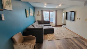 Ein Wohnzimmer mit einer Eckcouch, einem gemusterten Teppich und einem flachbildfernseher an der Wand.