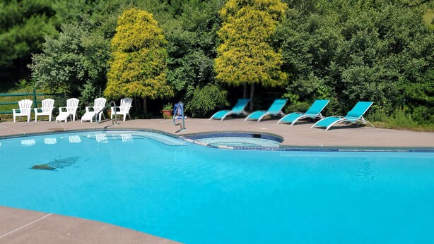 Ein Swimmingpool mit weißen und blauen Liegestühlen, umgeben von viel Grün.