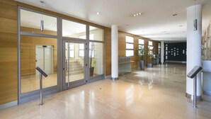 A spacious lobby with a modern design, featuring a glass entrance, a staircase, and a clean, polished floor. - Urumea | The Rentals Collection (San Sebastián/Donostia)