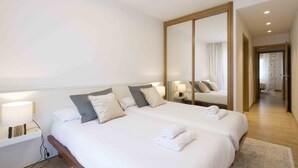 A hotel room with a large bed, bedside tables with lamps, a mirror, and a view of a hallway. - Urumea | The Rentals Collection (San Sebastián/Donostia)