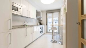 A modern kitchen with white cabinets, a granite countertop, stainless steel appliances, and a bar area with stools. - Urumea | The Rentals Collection (San Sebastián/Donostia)