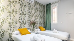 Una habitación de hotel con dos camas, una cortina verde, una ventana y un papel tapiz floral.