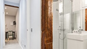 Un baño moderno con cabina de ducha de vidrio, un revestimiento de pared de madera y un lavamanos blanco con artículos de aseo.