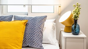 A neatly made bed with patterned pillows, a bedside lamp, and a vase with flowers. - Waou Anton Martin II - Alquiler Corta Duración (Madrid)