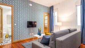 A modern living room with a patterned wallpaper, a flat-screen TV, a sofa, and a small table with a vase. - Waou Anton Martin II - Alquiler Corta Duración (Madrid)