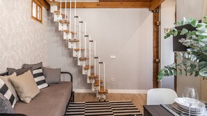 Ein modernes Wohnzimmer mit einer Holztreppe, einem Sofa mit gestreiften Kissen und einer Essecke mit Tisch für zwei Personen.