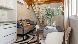 Ein gemütliches Zimmer mit einer Couch, einem Esstisch gedeckt mit Tellern und Gläsern, einer Topfpflanze und einer Treppe mit einem markanten Design.