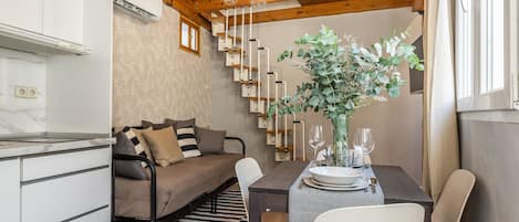 Una habitación acogedora con un sofá, una mesa de comedor dispuesta con platos y vasos, una planta en maceta y una escalera de diseño original.