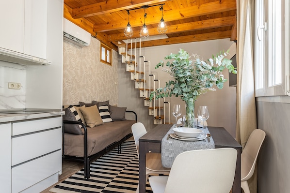 A cozy room with a sofa, dining table set with plates and glasses, a potted plant, and a staircase with a unique design.