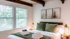 A bedroom with a bed, two bedside tables, a window with blinds, and three framed pictures on the wall.