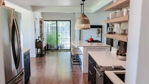 Una cocina moderna con un refrigerador de acero inoxidable, una isla central con taburetes y una lámpara colgante.