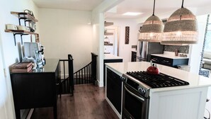 Una cocina moderna con una isla central, armarios negros, una estufa de acero inoxidable e iluminación colgante.