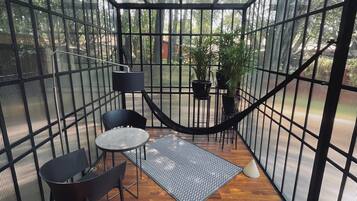 Un área de estar al aire libre cubierta, con suelo de madera, baranda de metal y plantas en macetas.