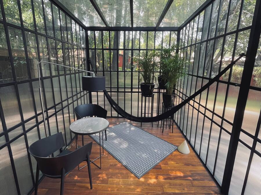 Un área de estar al aire libre cubierta, con suelo de madera, baranda de metal y plantas en macetas.