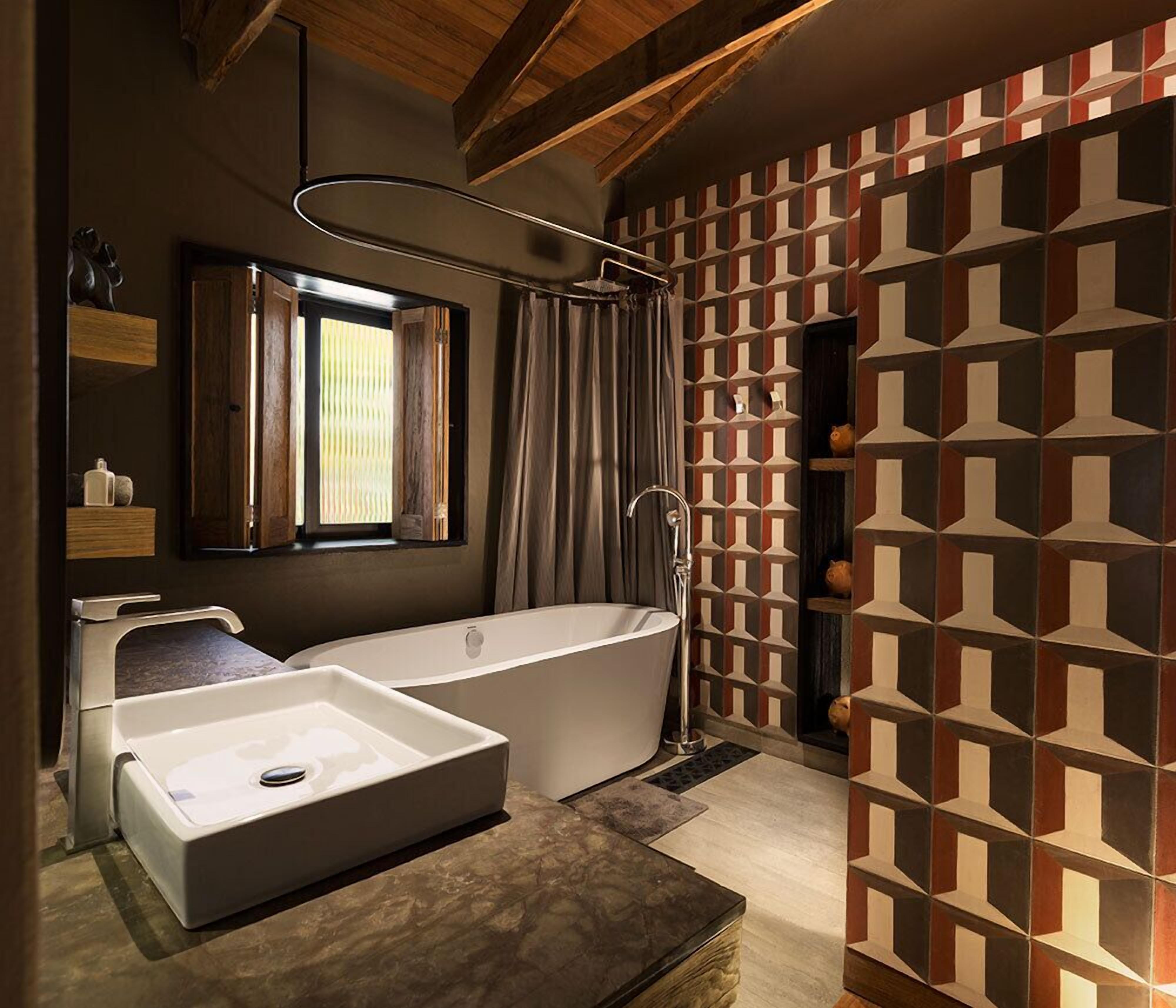 A modern bathroom with a freestanding bathtub, a large mirror, and a geometric-patterned wall.